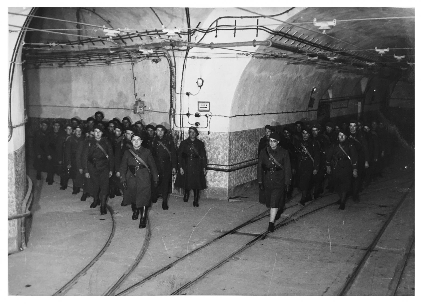Ligne Maginot - HACKENBERG - A19 - (Ouvrage d'artillerie) - Magasin M1, galerie de sortie des plateformes Péchot vides et accès à la gare principale. Noter la composition particulièrement 'cinématographique' de la photo : une telle arrivée en groupe synchronisé d'éléments issus du M1 et de la galerie de l'ouvrage avait peu de raison d'être dans la réalité... - Inconnu